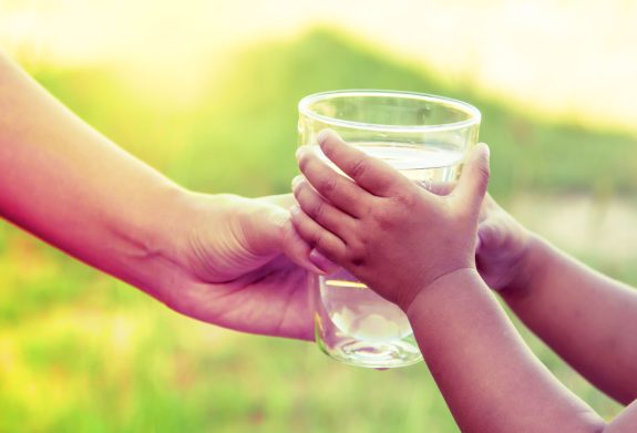 Glass of water being handed from adult to child